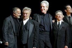 the men are all dressed up and posing for a group photo in black suits on stage