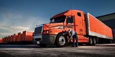 two men standing next to an orange semi truck