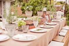 a long table set up with plates and vases on it for an outdoor dinner