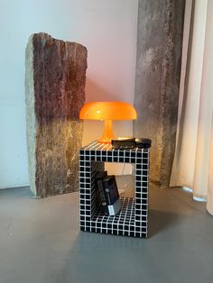 a lamp sitting on top of a table next to a book case and a rock