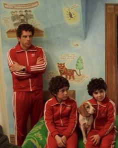 two boys and a dog are sitting on a bed in matching red tracksuits