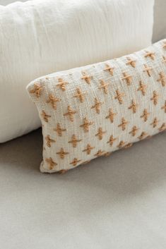 two pillows sitting next to each other on top of a white bedding set with orange crosses