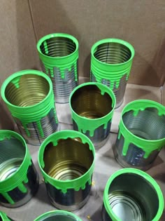 several green cups sitting on top of a cardboard box filled with tin cans and lids