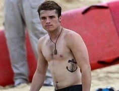 shirtless young man walking on the beach with an anchor tattoo on his chest and no shirt