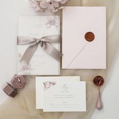 the wedding stationery is laid out with pink flowers and wax stamp on it's envelope