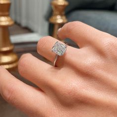 a woman's hand with a diamond ring on top of her finger, in front of a couch