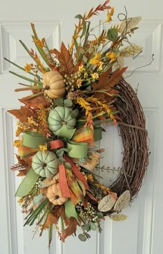 a wreath with pumpkins and leaves hanging on a door