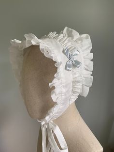 "This listing is for a made-to-order frilled cotton bonnet cap, suitable for periods c1820 to 1840. The cap is sized to fit adult heads from 21\" to 23\" - larger or smaller sizes available upon request. Inside the back of the cap is a drawstring and bow, to allow for adjustment on the head, and also to facilitate easier pressing after laundering. The cap is made from a light cotton lawn, and can be starched if you need to (I don't starch the caps myself). It features cotton bonnet strings (ties) to fasten to the head, and an optional satin bow detail, on either one side or both. The bow in the sample is blue, but other colours are available. There are two versions of the bonnet cap -machine sewn and hand sewn. The bonnet in the sample photos is machine sewn, but put together in a way that Adjustable Cotton Bonnet With Lace Trim, Adjustable Cotton Vintage Bonnet, Fitted Cotton Bonnet With Lace Trim, White Cotton Bonnet For Baptism, White Cotton Bonnet, One Size Fits Most, Adjustable White Hat With Ruffles, Adjustable White Ruffled Hat, Adjustable White Ruffle Hat, Adjustable Ruffled Bonnet