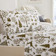 a bed with white and gold sheets covered in deer, trees and snowflakes