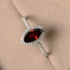 a ring with a pear shaped red stone surrounded by white diamonds on a beige background