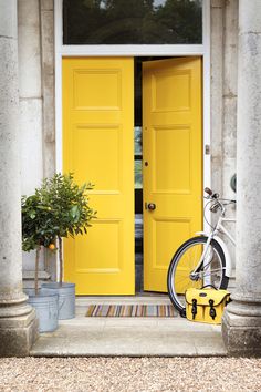 a bike parked in front of a yellow door with potted plants next to it