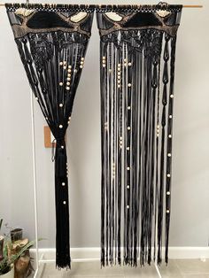 two black curtains with gold beading and fringes hanging on a wall next to a potted plant