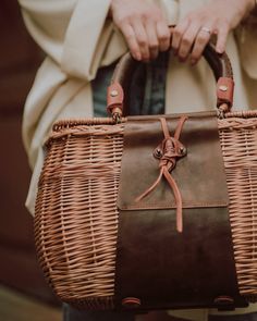 a woman holding a brown wicker basket with leather handles and straps on her shoulder