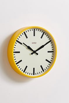 a yellow clock with black hands on a white wall above it is the time eleven o'clock