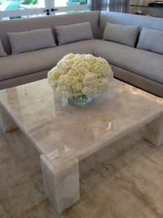 a white marble coffee table with flowers in a glass vase on the top and couches behind it