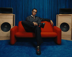 a man sitting on top of a red couch in front of two speaker's