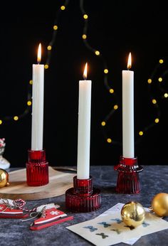 three lit candles on a table with christmas decorations