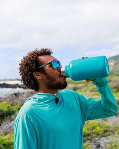 a man wearing sunglasses drinking from a blue water bottle