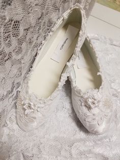 two pairs of white shoes sitting on top of a lace covered tablecloth next to each other