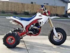 a red white and blue dirt bike parked on the sidewalk