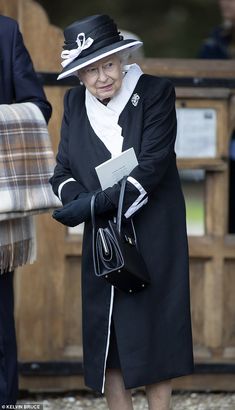 an older woman in a black coat and hat is holding her hand on her purse