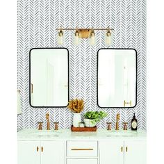 two mirrors on the wall in a bathroom with white cabinets and gold faucets