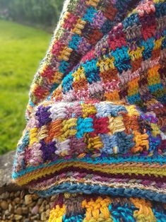 a multicolored crocheted blanket sitting on top of a pile of rocks