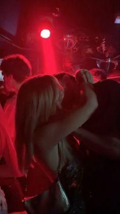 two people kissing in front of a red light at a club or bar with other people