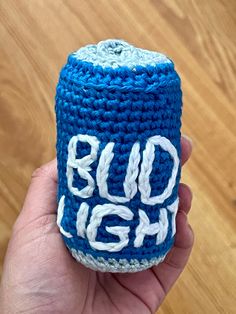 a hand holding a blue crocheted bud light can cozying toy with the words bud light written on it