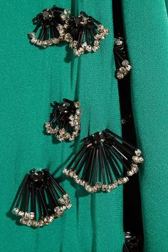 the back of a woman's green dress with black and silver brooches