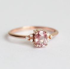 a pink diamond ring with three diamonds around it on a white surface, in front of a plain background