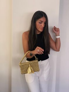 a woman in white pants and black top holding a handbag next to a wall