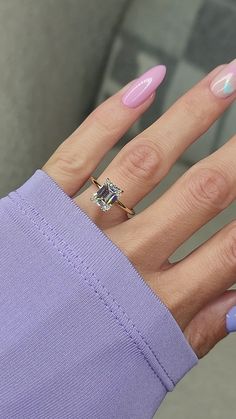 a woman's hand with pink and blue manicures holding an engagement ring