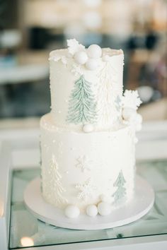 a three tiered cake with white frosting and pine trees on the top is sitting on a glass table