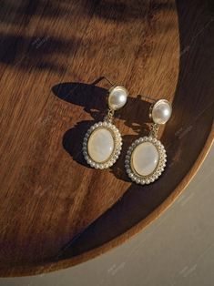 A pair of elegant vintage-inspired earrings featuring a delicate oval-shaped pendant adorned with a shimmering pearl border. The center of each pendant showcases a soft, white gemstone with a subtle pearlescent sheen. A second pearl is suspended from the top of each earring, adding a touch of classic sophistication. Material: Synthetic Opal, Synthetic Pearl Measurement: 0.6in Every purchase comes with a luxurious velvet pouch, a versatile accessory you can reuse for jewelry storage or travel, ma White Oval Pearl Earrings For Formal Occasions, Elegant Oval Pearl Earrings For Anniversary, Oval Pearl Earrings For Anniversary, Wedding Oval Pearl Earrings, Elegant Oval Pearl Earrings, Oval Pearl Drop Earrings In Pearl White, White Oval Party Earrings, Formal White Oval Pearl Earrings, Oval Pearl Charm Earrings For Wedding