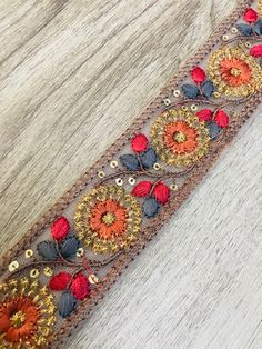 a close up of a piece of cloth with beads and flowers on it, sitting on a wooden surface