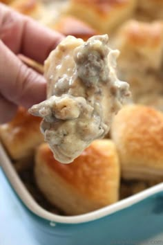 a hand holding a piece of bread with meat and cheese on it in a casserole dish