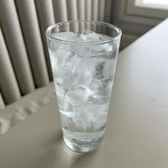 a glass filled with ice sitting on top of a white table next to a window