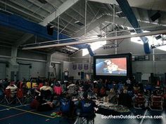 a large group of people sitting in chairs watching a movie on a big tv screen