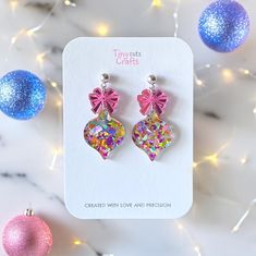 two pink heart shaped earrings with bows on them next to christmas ornaments and glitter balls