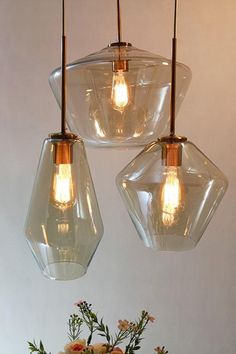 three clear glass pendant lights hanging over a vase with flowers in it on a table