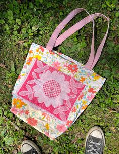 someone's feet are standing next to a pink and white bag on the grass