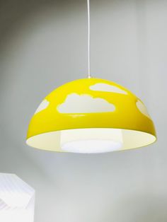 a yellow lamp hanging from a ceiling with clouds painted on the lampshade above it