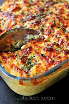 a casserole dish with cheese and herbs being scooped from the casserole