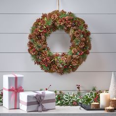 a wreath with pine cones and evergreens is hung on the wall next to presents