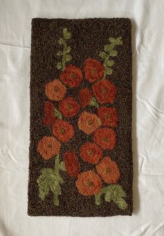 an orange and brown rug with flowers on it sitting on top of a white sheet