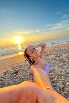 a woman laying on top of a sandy beach next to the ocean at sun set