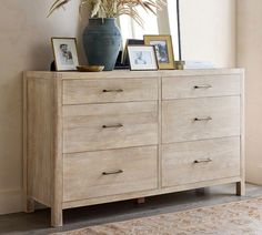 a wooden dresser with pictures on top and a potted plant sitting on top of it