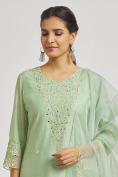 Mint green A-line kurta with floral vine and mirror work embroidery. Comes with embroidered hem pant and dupatta.
Components: 3
Pattern: Embroidered
Type Of Work: Floral Vine
Neckline: Round
Sleeve Type: Three Quarter
Fabric: Organza, Muslin, Chanderi
Color: Green
Other Details: 
Attached lining
Back elasticated pant waistband
Length:
Kurta: 48
Pant: 37
Approx. product weight: 1 kg
Occasion: Puja - Aza Fashions Kurta Pant Set, Embroidered Hem, A Line Kurta, How To Hem Pants, Kurta With Pants, Floral Vine, Mirror Work, Pant Set, Set For Women