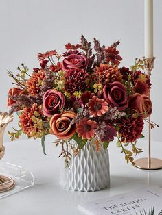 a white vase filled with lots of flowers on top of a table next to a candle